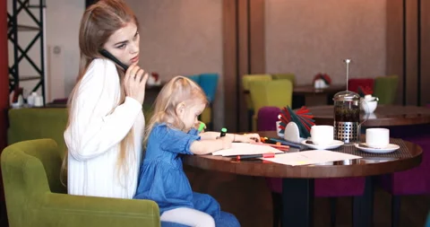 Daughter draws while mom is talking on the phone. Mom and daughter in a cafe. Video stock 167077715
