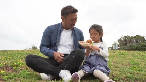 A Daughter Eating a Hamburger While Smiling and Gazing at Her Father in the Stock Footage 333185476