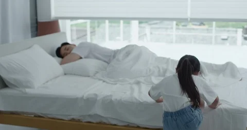 Daughter jumping on bed to wake up sleeping dad Stock Footage 100938600