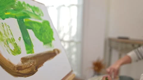 The daughter is painting on an easel, using the hand painting technique Video stock 338430737