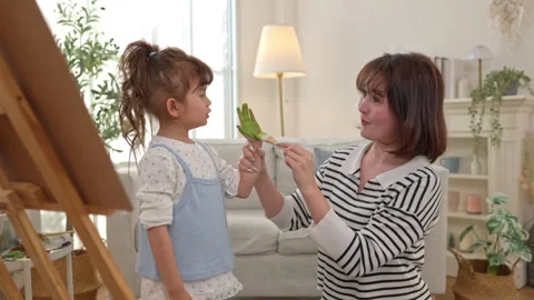 The daughter is painting on an easel, using the hand painting technique Video stock 338430818