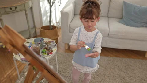The daughter is painting on an easel, using the hand painting technique Stock Footage 338430856