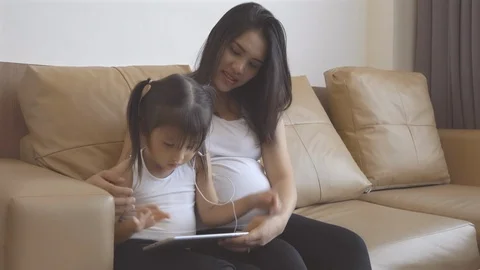 Daughter playing tablet computer with pregnant mother belly in the living room. Stock Footage 115876682
