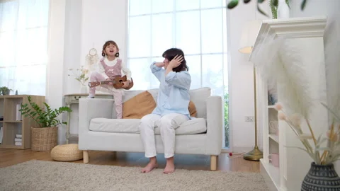 Daughter playing ukulele beside, creating a musical learning environment even Stock Footage 339578469