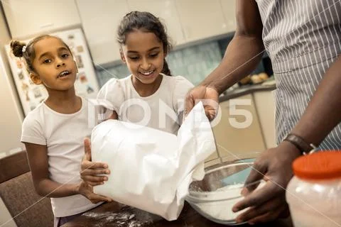 Daughters feeling cheerful and memorable while cooking with father Stock Photos