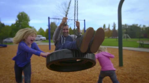 Daughters push dad around on a tire swing Stock Footage 58482048