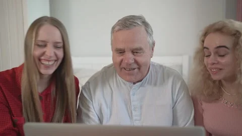Daughters visit old father, using laptop sitting on sofa. They talk, discuss web Stock Footage 278272113