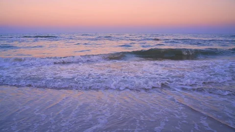 Dawn on the beach. Sea waves roll on the sandy beach. The pink sky is reflect Stock Footage 129181760