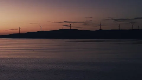 Dawn Wind Turbines over Calm Lake with Pink Glow Tracking Left 4K Stockbeeldmateriaal 343319014