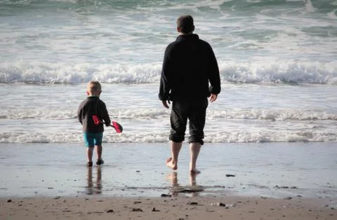 A day at the beach. Father and son walking towards the waves Stock Photos