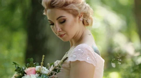 Day dreaming bride - blonde in pink dressand with tattoo poses with bouquet of Stock Footage 65502352