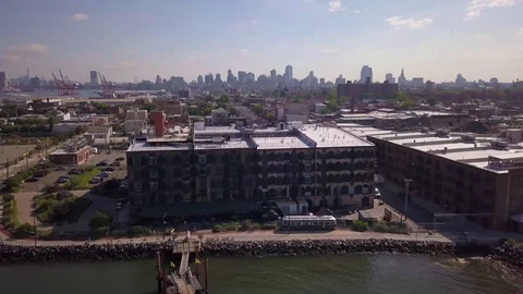 Day orbiting around Red Hook Brooklyn warehouse revealing Manhattan skyline Stock Footage