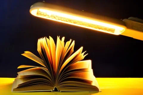 Daylight lamp, illuminates the book on the table in the dark. Stock Photos