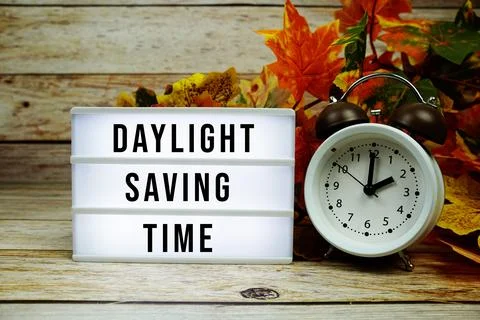 Daylight Saving Time text with alarm clock and maple leaf decoration on woo.. Stock Photos