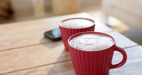Daylight shifting is casting highlights on two red mugs of frothy coffee to Stock Footage 336715395