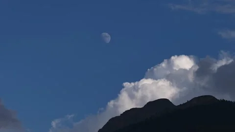 Daytime moon hanging in the blue sky over a mountain silhouette Stock Footage 318278076