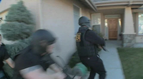 DEA officers with arms drawn perform a drug raid on a house. Stock Footage