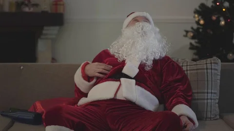 Dead drunk senior man in Santa Claus costume sitting on couch and drinking Stock Footage 120912484