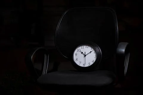 Deadline concept, time management. Clock on an office chair on a black backgr Stock Photos
