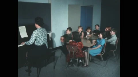 Decade: Students sitting at desks sing along with teacher playing on piano. Stock Footage 188531050