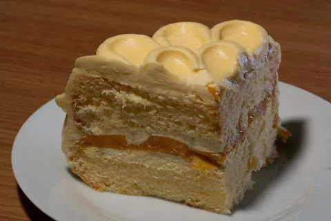 A Decadent Slice of Mango Layered Cake Topped with Swirls of Creamy Yellow .. Stock Photos