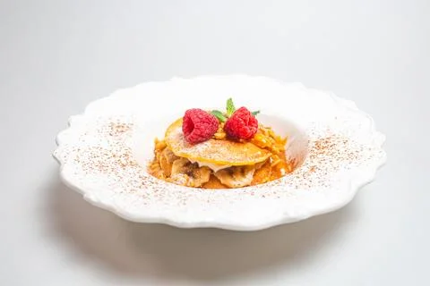 A decadent stack of pancakes topped with bananas, raspberries, and maple syru Foto stock