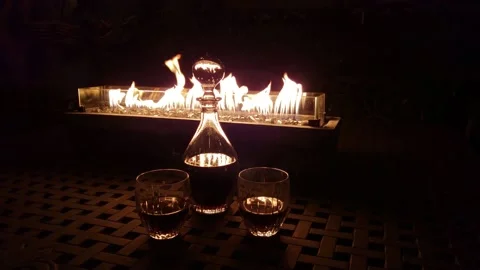 Decanter and two glasses in front of rectangular fire pit at night 4K. 库存影片 151653708