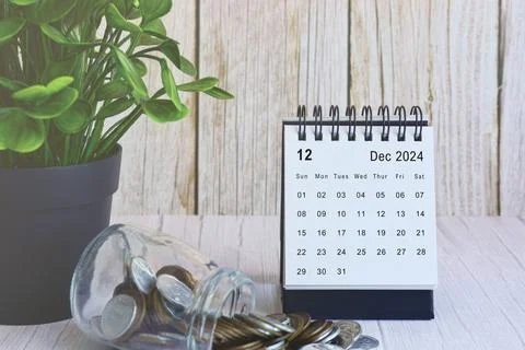December 2024 desk calendar with stack of coins and potted plant on wooden desk. Stock Photos
