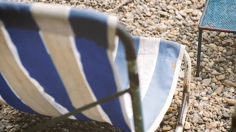 Deck chairs are blown by the wind on a pebble beach Stock Footage 113665501