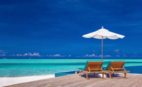 Deck chairs with umbrella overlooking infinity pool and lagoon Stock Photos