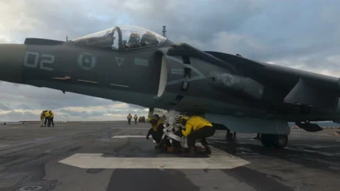 Deck crew secure steel tie downs to AV-8B Harrier II aboard USS Kearsarge LHD 3 Stock Footage 227138134