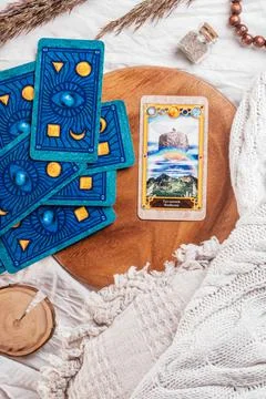 Deck of Tarot spread with one open card on wooden tray on white cloth sheet w Stock Photos