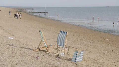 Deckchairs on Southend beach close to the sea, people are walking on the sand Stock Footage 129693416