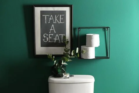 Decor elements, paper rolls and toilet bowl near green wall. Bathroom interio Stock Photos