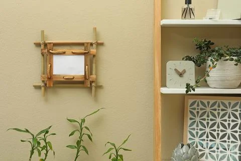 Decor elements on shelving unit near beige wall with bamboo frame indoors 写真素材
