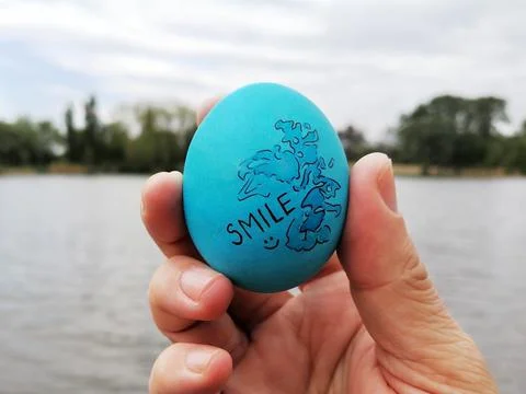 Decorated blue Easter egg with illustration and text smile in hand Stock Photos