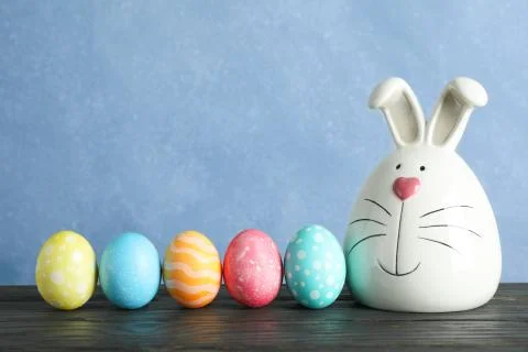 Decorated bunny and Easter eggs on table against color background. Space for  Stock Photos