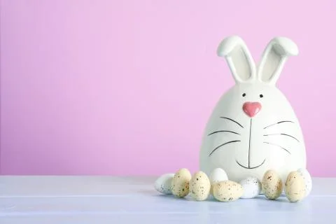 Decorated bunny and Easter eggs on table against color background. Space for  Stock Photos