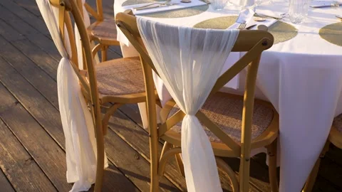 Decorated chairs with white drapes set around a table on a wooden deck at an Stock Footage 345283756