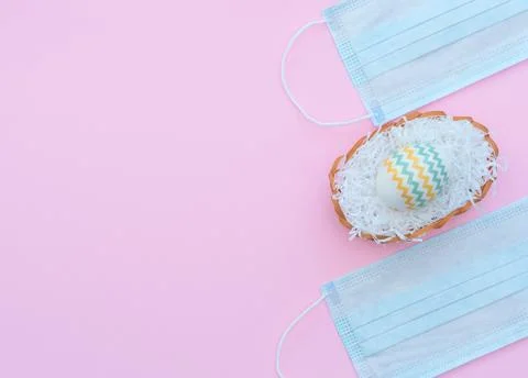 Decorated Easter egg in the basket and medical face masks on the pink backgro Stock Photos