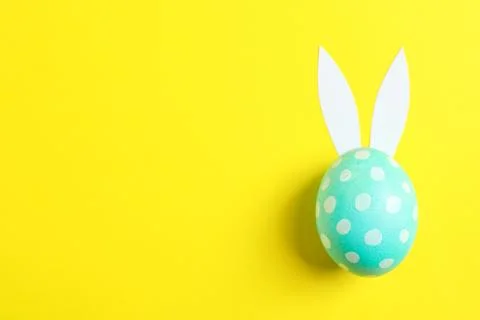 Decorated Easter egg with cute bunnies ears on yellow background. Space for t Stock Photos
