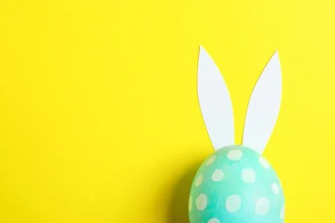 Decorated Easter egg with cute bunnies ears on yellow background. Space for t Stock Photos