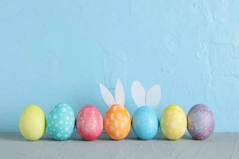 Decorated Easter eggs and cute bunny's ears on table against color background Foto stock