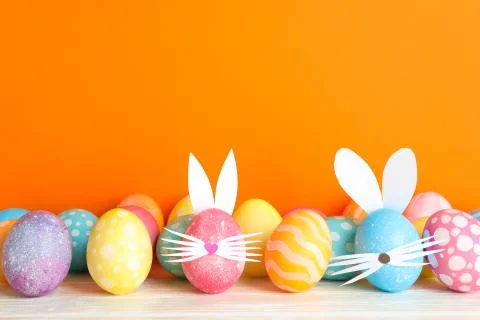 Decorated Easter eggs and cute bunny's ears on table against color background Foto stock