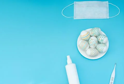 Decorated Easter eggs lie on the plate, medical face mask, thermometer and sa Stock Photos
