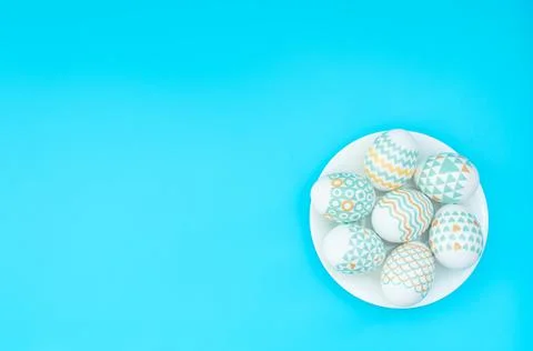 Decorated Easter eggs lie on the white plate on blue background. Happy Easter Stock Photos