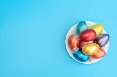 Decorated Easter eggs with small feathers lie on the plate on blue background Stock Photos