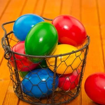 Decorated Easter eggs in wire basket on rustic wooden background Stock Photos