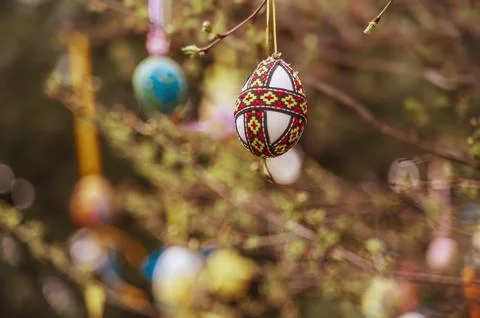 Decorated red Easter egg with traditional folk patterns hanging on a spring Stock Photos