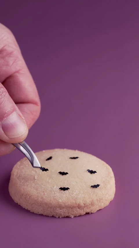 Decorating Halloween cookie with chocolate bat using tweezers on purple Stock Footage 341698159